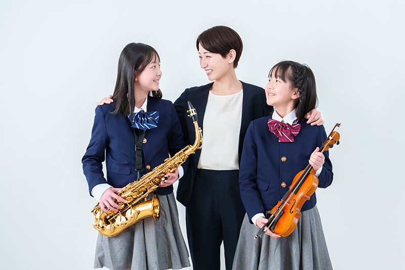 制服姿の女子生徒がバスケットボールを持ち、保護者らしき大人と笑顔で並んでいる。